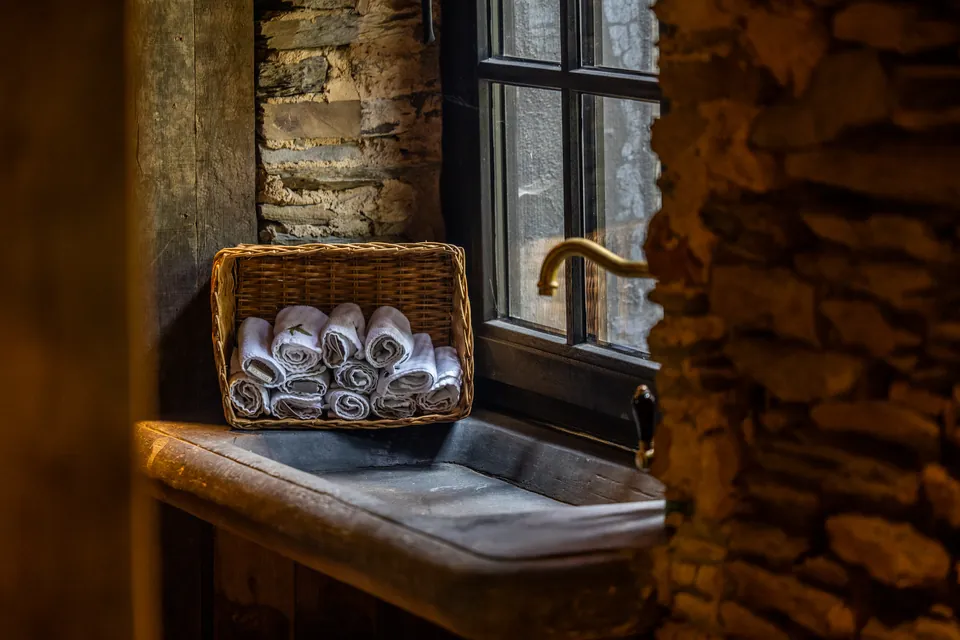 A basket of rolled towels beside a stone basin and window