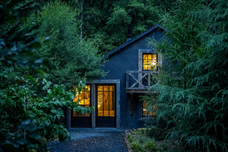 A warmly lit building surrounded by woodland at dusk